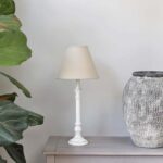 Antique white tablel lamp with linen shade on a table next to a pot.